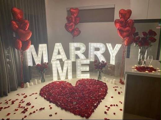 Romantic marriage proposal setup with heart balloons, petals and illuminated letters